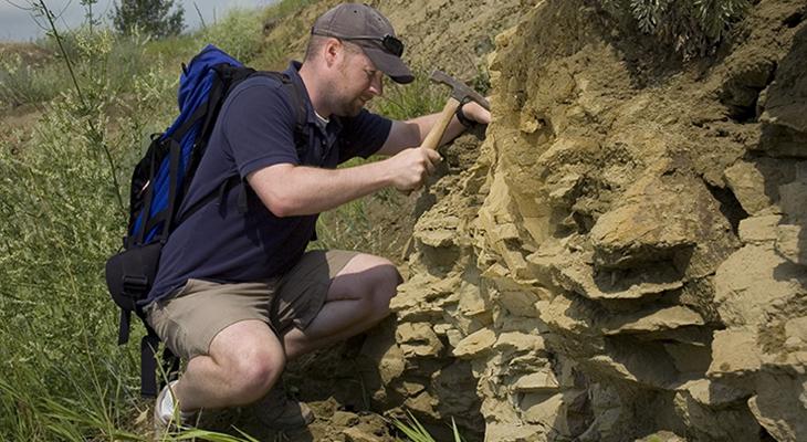 Craig Scott uses a rock hammer at a fieldwork site.